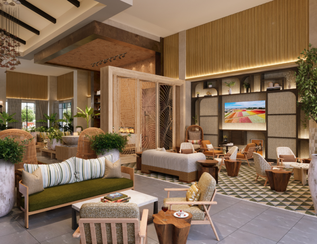 A modern hotel lobby with warm wood tones, comfortable seating, large plants, pendant lighting, a fireplace feature, and a wall-mounted TV displaying colorful art.