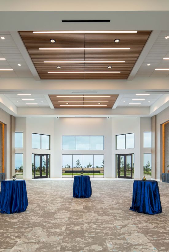 A spacious, modern event hall with high ceiling, recessed lighting, and three round tables draped in blue cloth, ready for a reception.