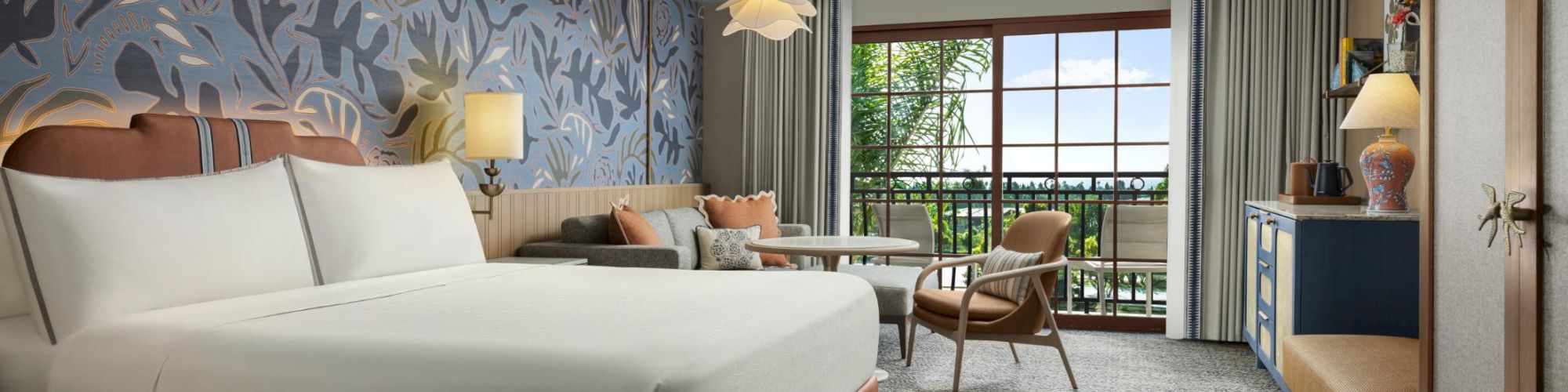 A stylish hotel room with a large bed, floral wallpaper, seating area, and a balcony view. 140 characters, ending with a period.