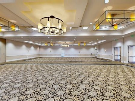 A large, empty conference hall with patterned carpet, bright ceiling lights, and wall sconces along the sides, ready for an event.