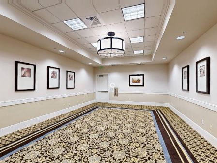 A spacious hallway or gallery with framed pictures on the walls, a patterned carpet, and a circular ceiling light fixture.