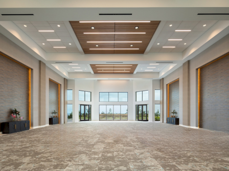 A spacious, modern conference or event hall with large windows, decorative ceiling panels, neutral tones, and ample natural light.