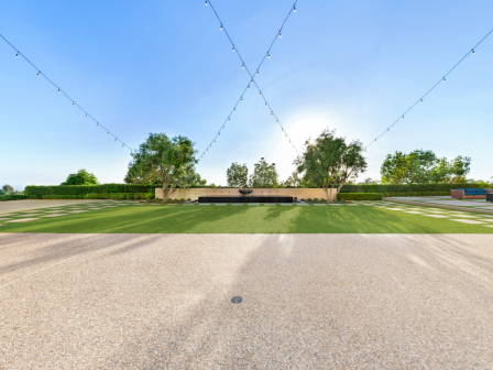 A wide, sunny outdoor area with string lights overhead, green lawns in a checkerboard pattern, trees in the distance, and a gravel path leading forward.