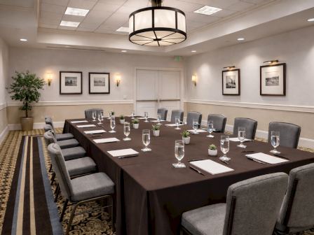 A modern conference room set with a long table, gray chairs, glassware, framed photos, and a ceiling chandelier.