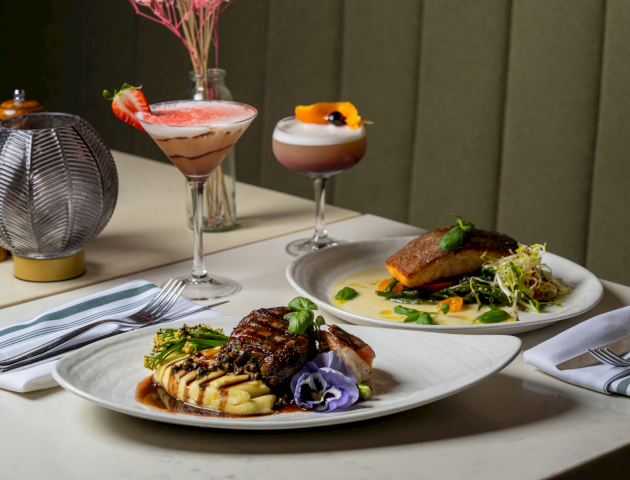 A plated gourmet meal with a colorful vegetable-topped main, side dishes, and a glass of wine at an upscale restaurant.