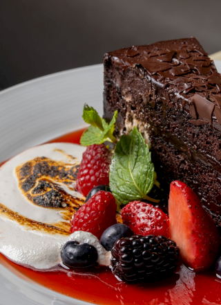 A slice of chocolate cake topped with berries and mint sits on a plate of red berry sauce.