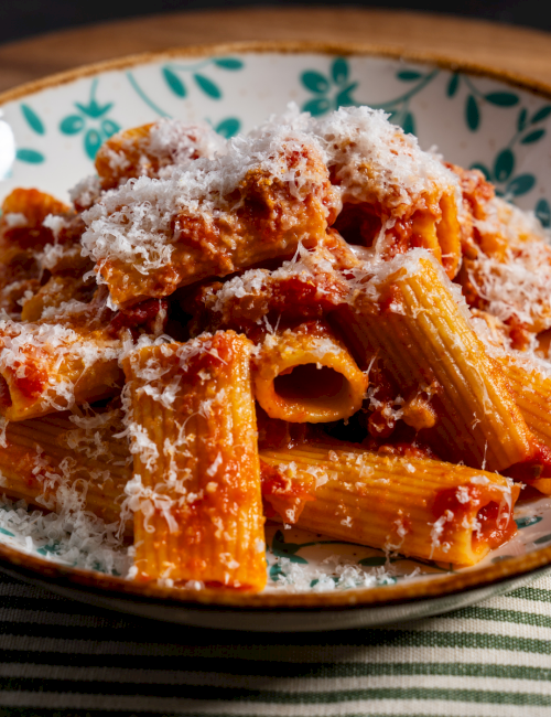 Pasta in a creamy tomato sauce, sprinkled with grated cheese, served in a floral bowl on a striped placemat.
