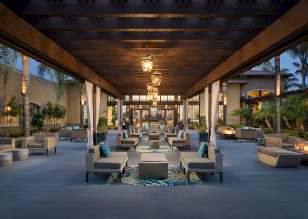 A luxurious outdoor lounge area with comfy seating, low tables, and warm lighting under a covered pergola, perfect for evening gatherings.