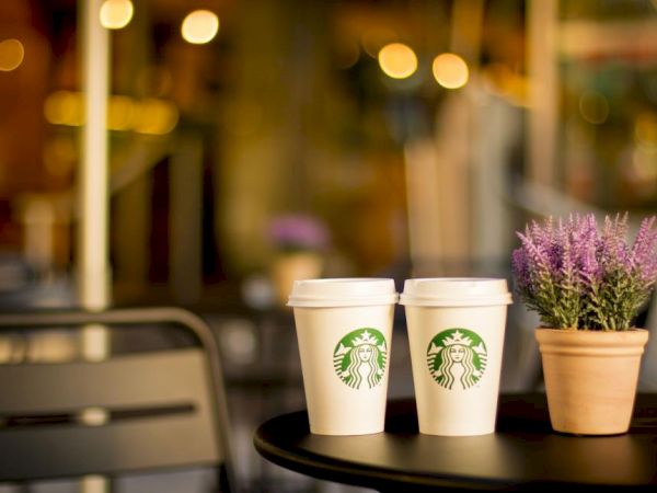 Two Starbucks cups on a small table beside a lavender plant, blurred city lights in the background.