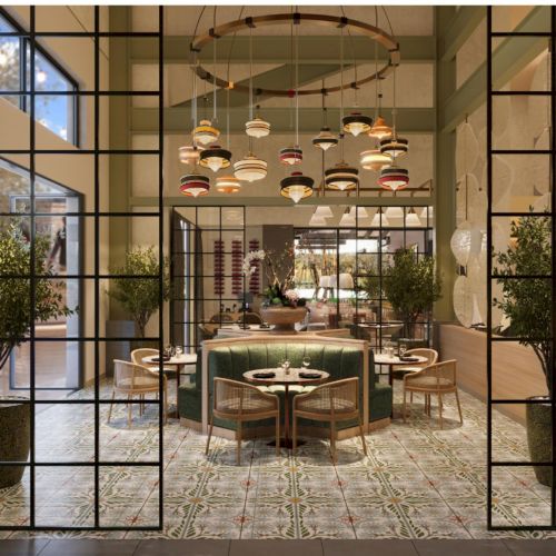 A stylish restaurant interior seen through a black grid door: warm lighting, hanging lamps, green plants, and a central round dining table setup.