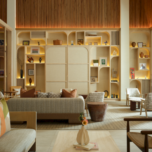 A stylish, sunlit living room with built-in curved shelving, cozy cream sofas, woven chairs, and warm wood accents creating a welcoming, modern lounge.