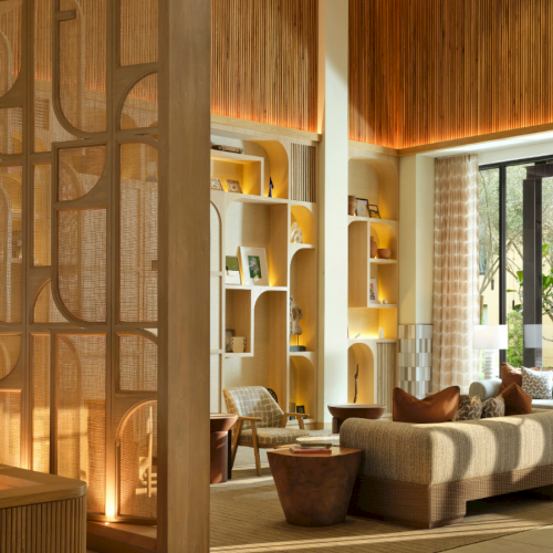 Luxurious hotel lobby with warm wood tones, modern shelving, cozy seating, and natural light from large windows.