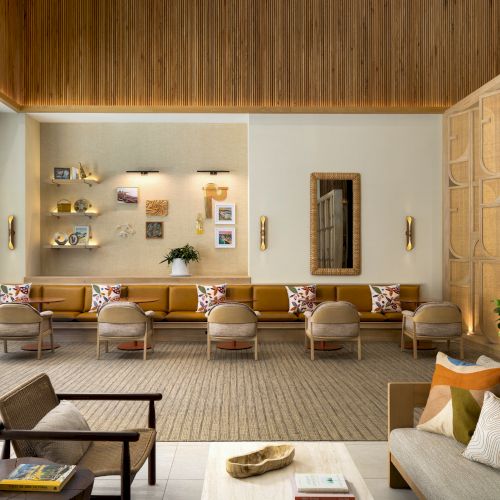 A modern, open living room and kitchen with wooden shelves, warm lighting, a couch, table, and potted plants.