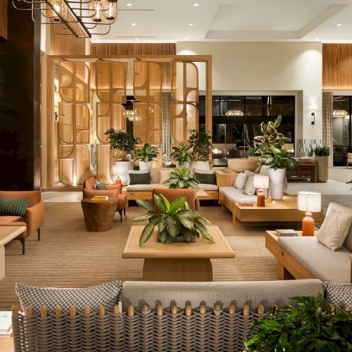 Cozy living room with warm lighting, plants, couches, and a coffee table; open shelves and soft decor create a welcoming, lived-in vibe.