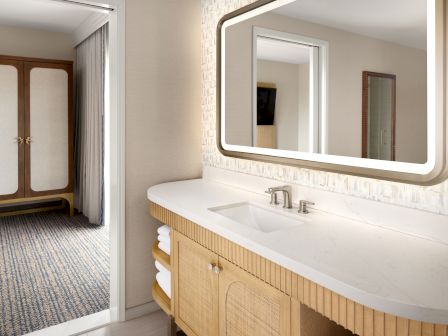 Modern bathroom vanity with double sink, sleek illuminated mirror, stone counter, and wood cabinetry in a bright suite.