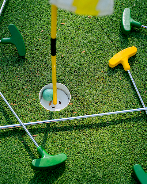 A mini golf setup with colorful plastic tees and rods on a green turf, surrounding a hole with a flag.