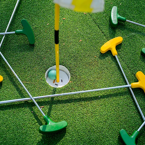 A mini golf setup with colorful plastic tees and rods on a green turf, surrounding a hole with a flag.