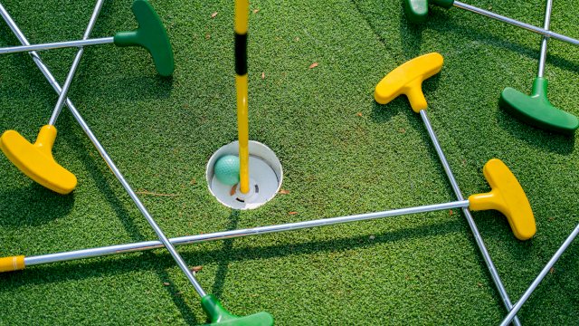 A mini golf setup with colorful plastic tees and rods on a green turf, surrounding a hole with a flag.
