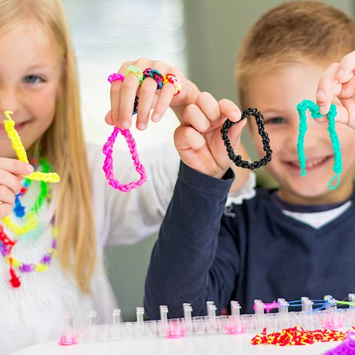 Two kids show off colorful bracelets they made with bright beads and strings, smiling proudly at their craft project.
