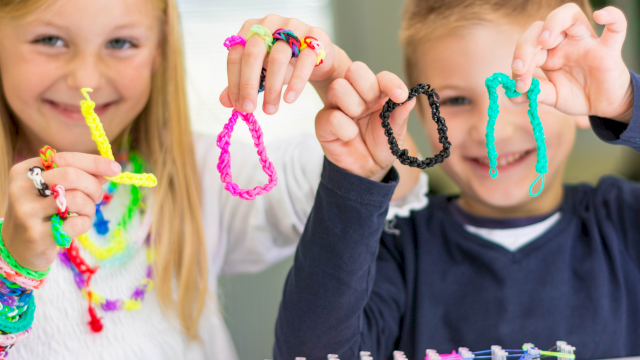 Two kids show off colorful bracelets they made with bright beads and strings, smiling proudly at their craft project.