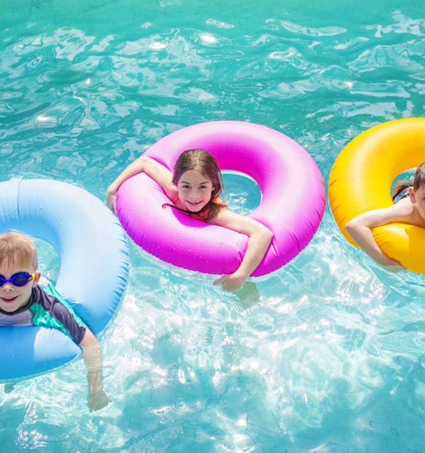 Three kids float on colorful inner tubes in a sunny pool, smiling and relaxing in the crystal-clear water.