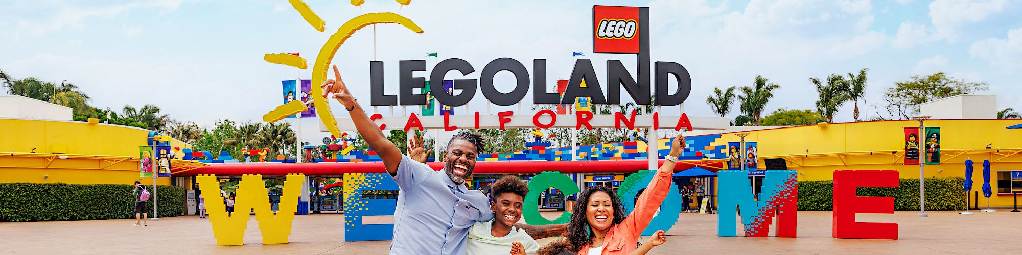 Cheerful family posing at LEGOLAND California, with giant LEGO letters and bricks in a sunny outdoor park.