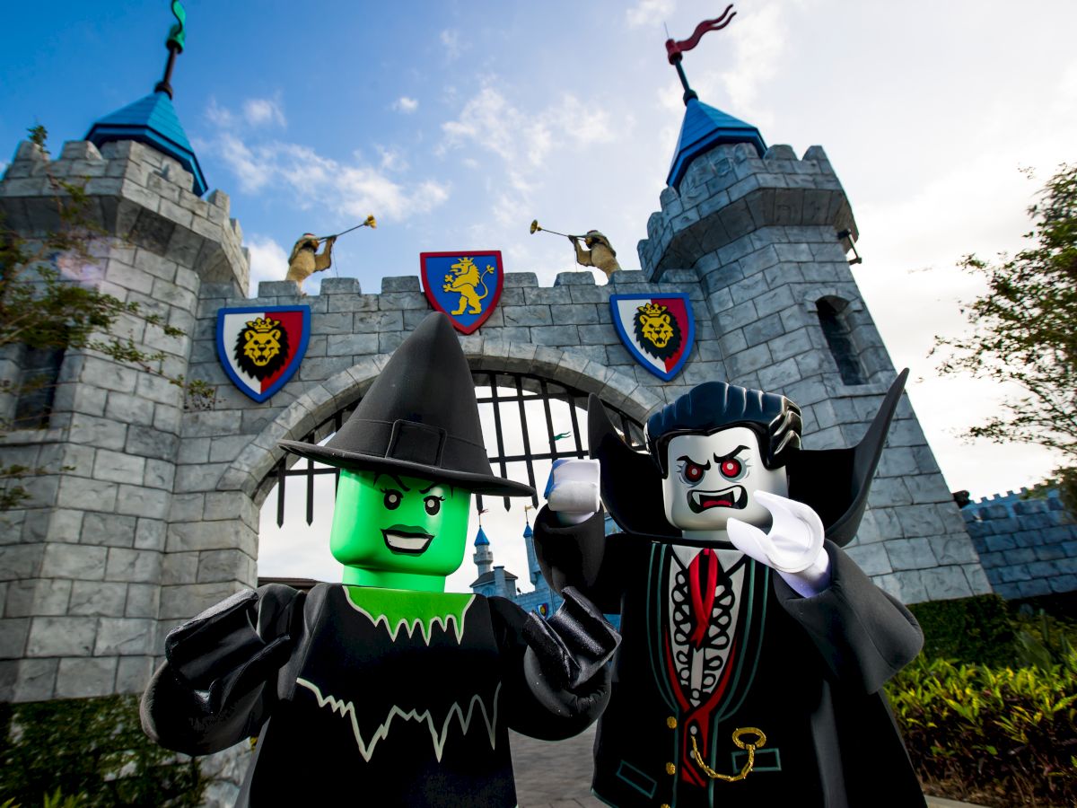 Two LEGO-like wizards in front of a stone castle wall with roaring-lion emblems on banners under a blue sky.