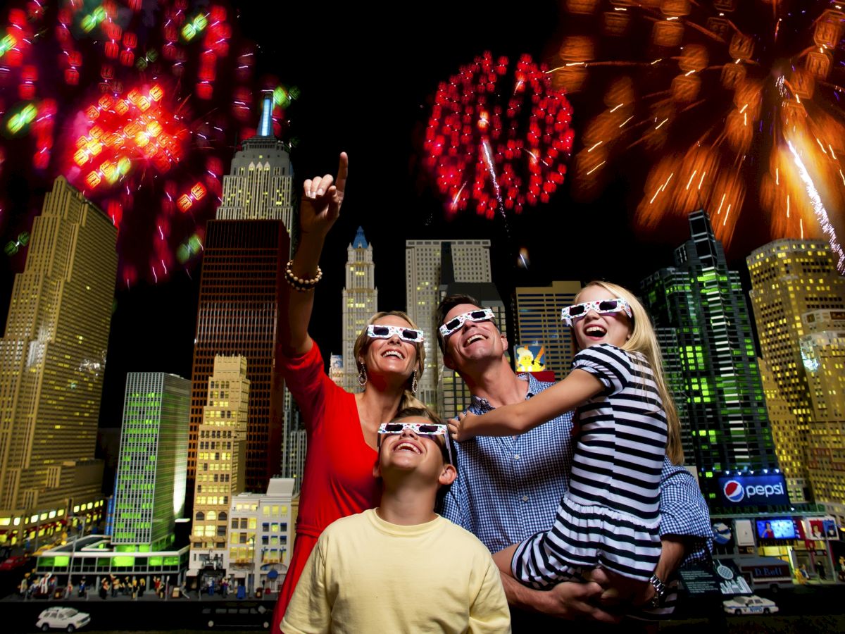 At night in a city, a family wearing 3D glasses cheers as fireworks light up the skyscrapers.