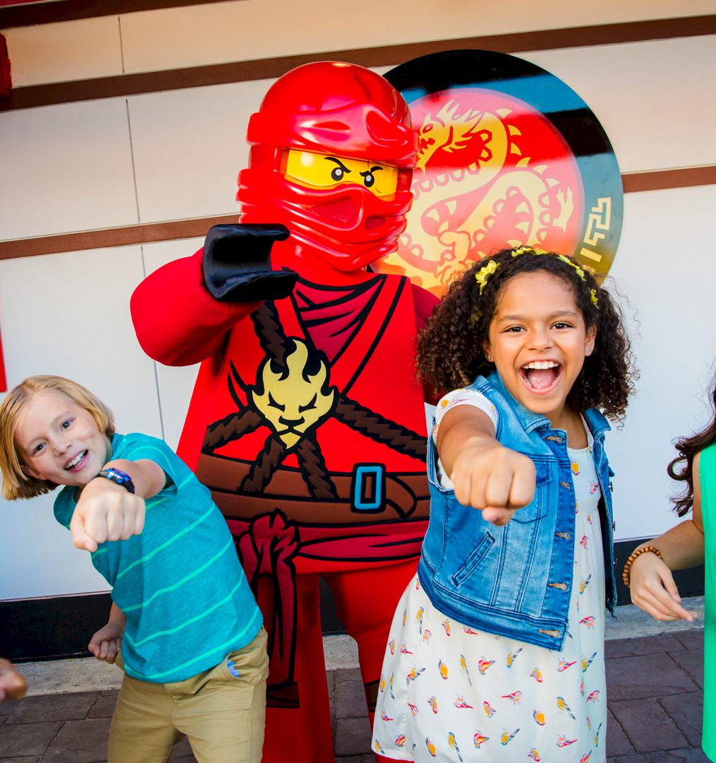 Kids grin and point at the camera beside a red ninja Lego-style mascot at a party!