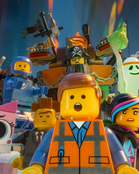A crowd of LEGO-style characters in colorful armor and masks, including a pirate hat, cheering on stage.
