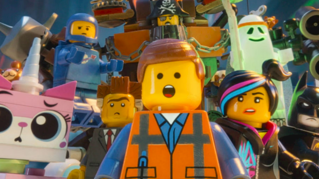 A crowd of LEGO-style characters in colorful armor and masks, including a pirate hat, cheering on stage.
