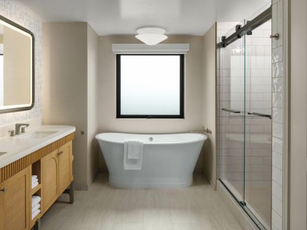 Bright modern bathroom with a freestanding tub, tiled shower, vanity sink, towel rack, and large window.