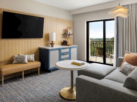 A bright living room with a sofa, TV on a wood wall, blue console, coffee table, and a large sliding door to a balcony.